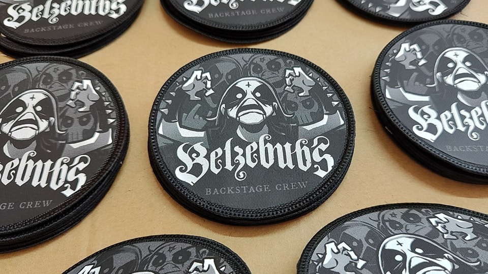 Okrągłe naszywki z logo zespołu Belzebubs i napisem 'Backstage Crew', czarno-białe wzory na szarym tle, widoczne detale haftu na obrzeżach.