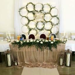 Sweet Times - Dekoracja stołu prezydialnego na uroczystość: złoty cekinowy obrus, girlanda z białych kwiatów i zieleni, tło z białej tkaniny z obręczami oplecionymi zielenią i lampkami, świeczniki i lampiony.