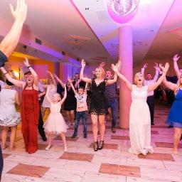 Sweet Times - Rozbawiona grupa gości weselnych tańczy z podniesionymi rękami na parkiecie, oświetlona dyskotekową kulą i kolorowymi światłami, z widocznym mężczyzną w kapitańskim stroju z przodu.