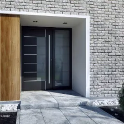 Nowoczesne drzwi wejściowe z czarnym panelem i szybą, wkomponowane w elewację z szarej cegły i drewnianą okładziną, z małymi drzewkami iglastymi po bokach.