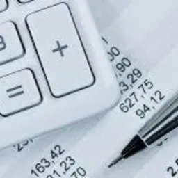 Kalkulator i metalowy długopis na wydruku z danymi finansowymi, widoczne liczby i symbole matematyczne.