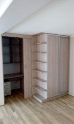 Szafa wnękowa z przesuwnymi drzwiami i biurkiem w zabudowie, z jasnego drewna, dopasowana do skosu dachu, Rychwał.
