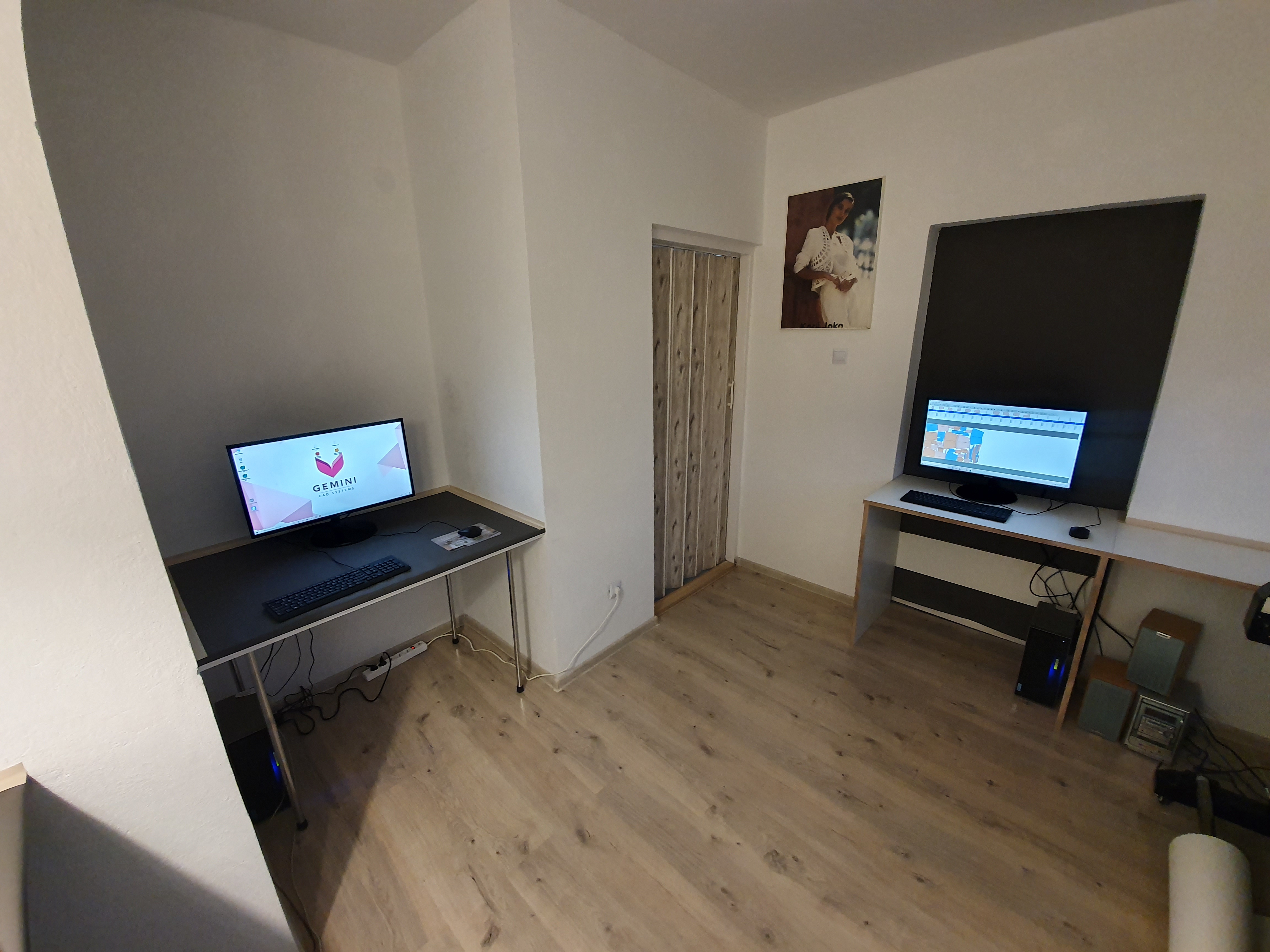 Dwa stanowiska komputerowe w jasnym pomieszczeniu, jedno z oprogramowaniem CAD, drugie z mapą, na ścianie plakat z kobietą.