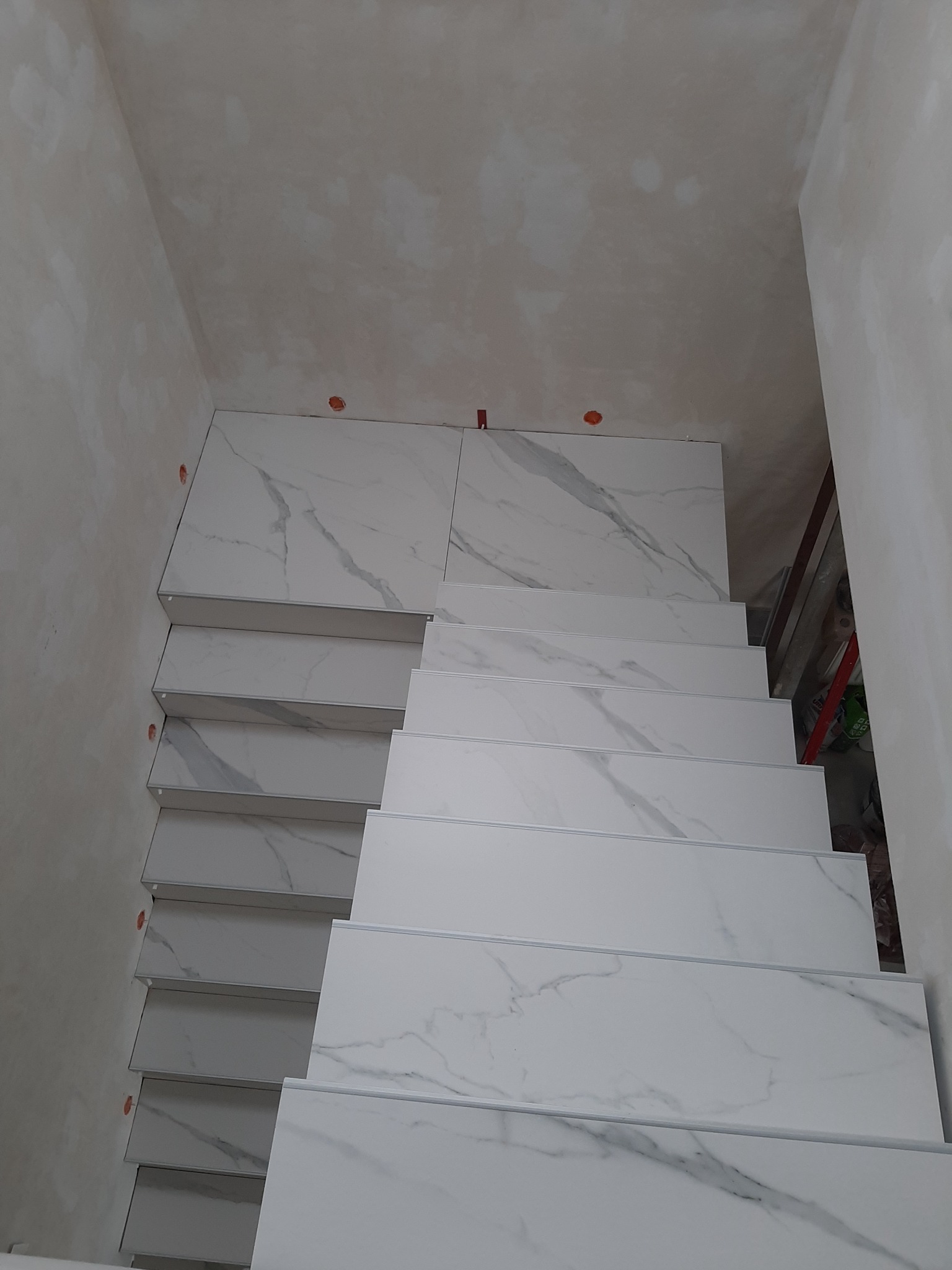 Schody wyłożone białymi płytkami imitującymi marmur, widok z góry, ściany surowe, przygotowane do wykończenia.