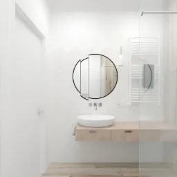 Minimalistyczna łazienka z okrągłym lustrem, białą umywalką na drewnianej szafce, grzejnikiem drabinkowym i białymi płytkami ułożonymi w jodełkę.