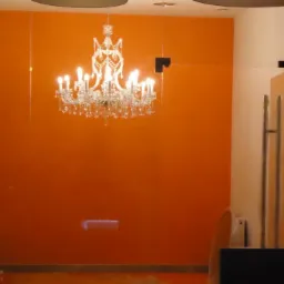 Kryształowy żyrandol zawieszony na tle pomarańczowej ściany, widoczne elementy szklanej zabudowy i wieszak na ubrania.