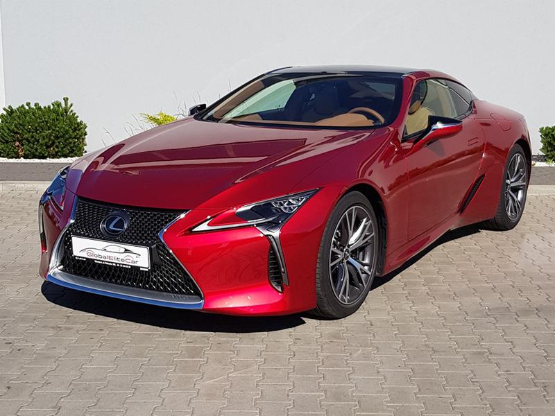 Błyszczący, wiśniowy Lexus LC 500 z beżowym wnętrzem, prezentowany na zewnątrz z logo wypożyczalni samochodów na przednim grillu.