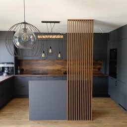 TDM - Nowoczesna kuchnia w odcieniach szarości z drewnianymi akcentami, wyspą i ażurową ścianką działową z pionowych listew, oświetlona wiszącymi lampami z żarówkami Edison oraz lampą kulą.