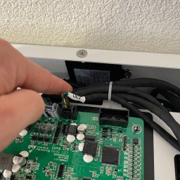 Solcity - Fotowoltaika i Systemy Grzewcze - Szczegółowe ujęcie zielonej płytki drukowanej z elektroniką wewnątrz białej obudowy, z palcem wskazującym na złącze kablowe z czarno-żółto-zielonymi przewodami.