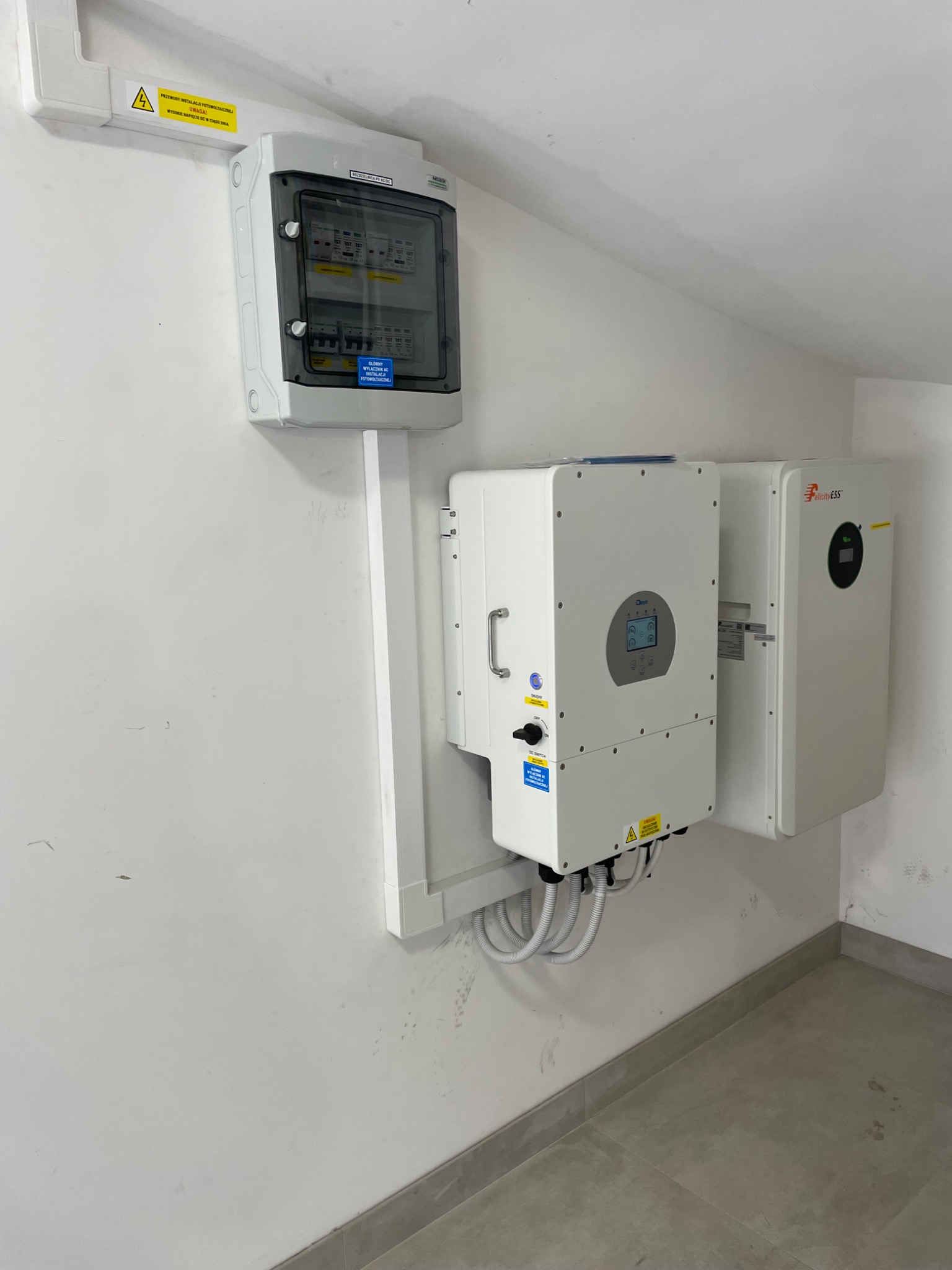 Zainstalowany system zasilania awaryjnego: falownik Deye i magazyn energii Felicity ESS zamontowane na ścianie, z widoczną skrzynką bezpieczników i okablowaniem.