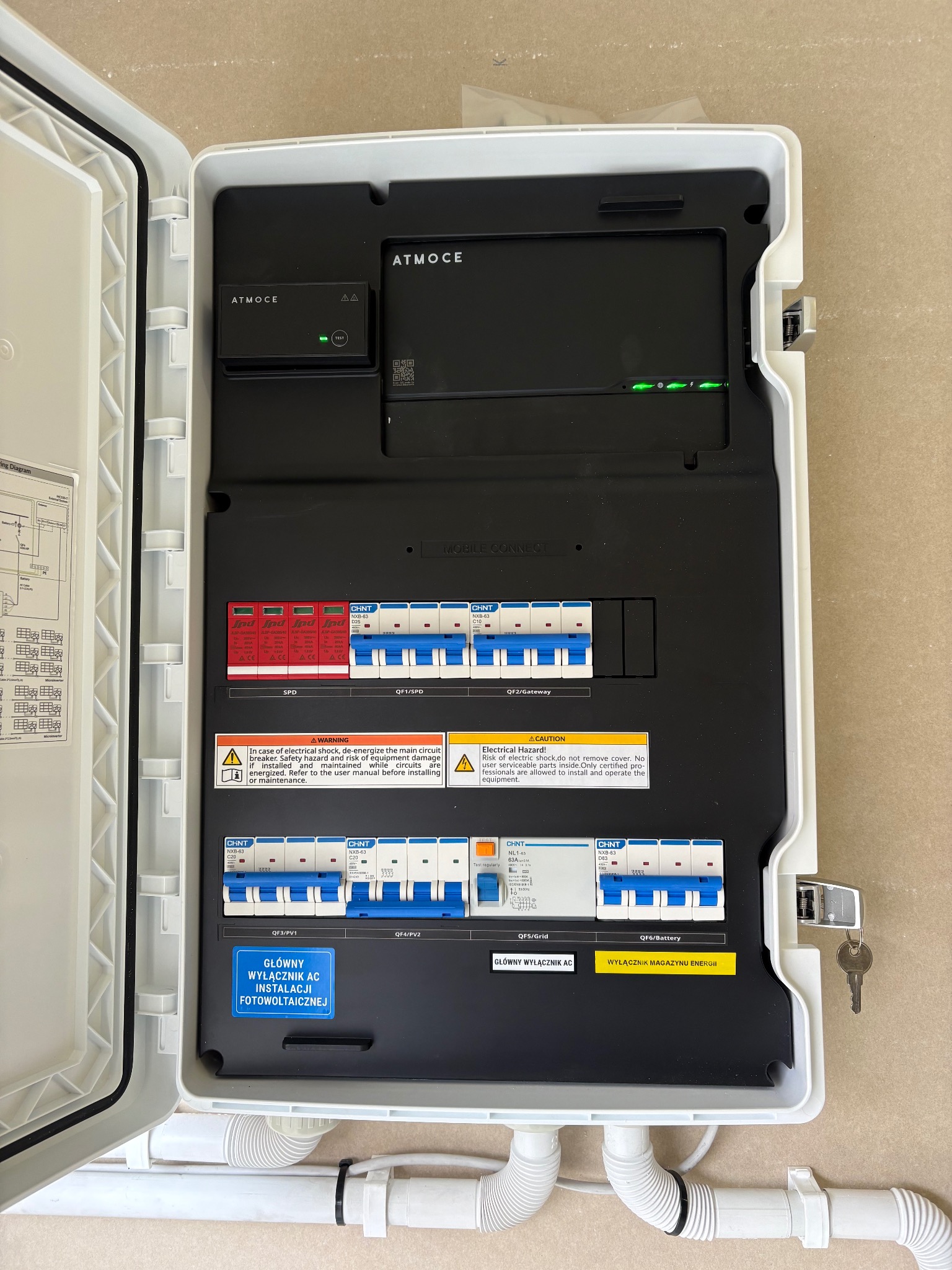 Otwarta skrzynka z bezpiecznikami i modułem sterującym instalacji fotowoltaicznej marki Atmoce, z widocznymi zabezpieczeniami SPD i wyłącznikami, kluczyk w zamku.