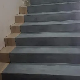 Schody wyłożone szarą płytką z drewnopodobnymi podstopnicami, widoczne niedociągnięcia na ścianie.