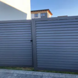 Nowoczesna, przesuwna brama wjazdowa z poziomymi panelami w odcieniach szarości, z widocznym zamkiem i fragmentem posesji w tle.