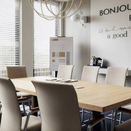 Aranżacja, projektowanie wnętrz MIA PROJEKT Maria Leśna - Jasna sala konferencyjna z drewnianym stołem i krzesłami. Na ścianie napis 'Bonjour Paris' i grafika wieży Eiffla. Nowoczesne oświetlenie i rolety w oknach.