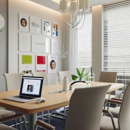 Aranżacja, projektowanie wnętrz MIA PROJEKT Maria Leśna - Jasna sala konferencyjna z drewnianym stołem, krzesłami i laptopem. Na ścianie zegary stref czasowych i grafiki. Żaluzje w oknach wpuszczają delikatne światło.