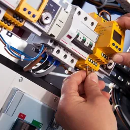 Podłączenie przewodów do żółtego modułu w rozdzielnicy elektrycznej, widoczne zabezpieczenia i kable w kolorowych izolacjach.