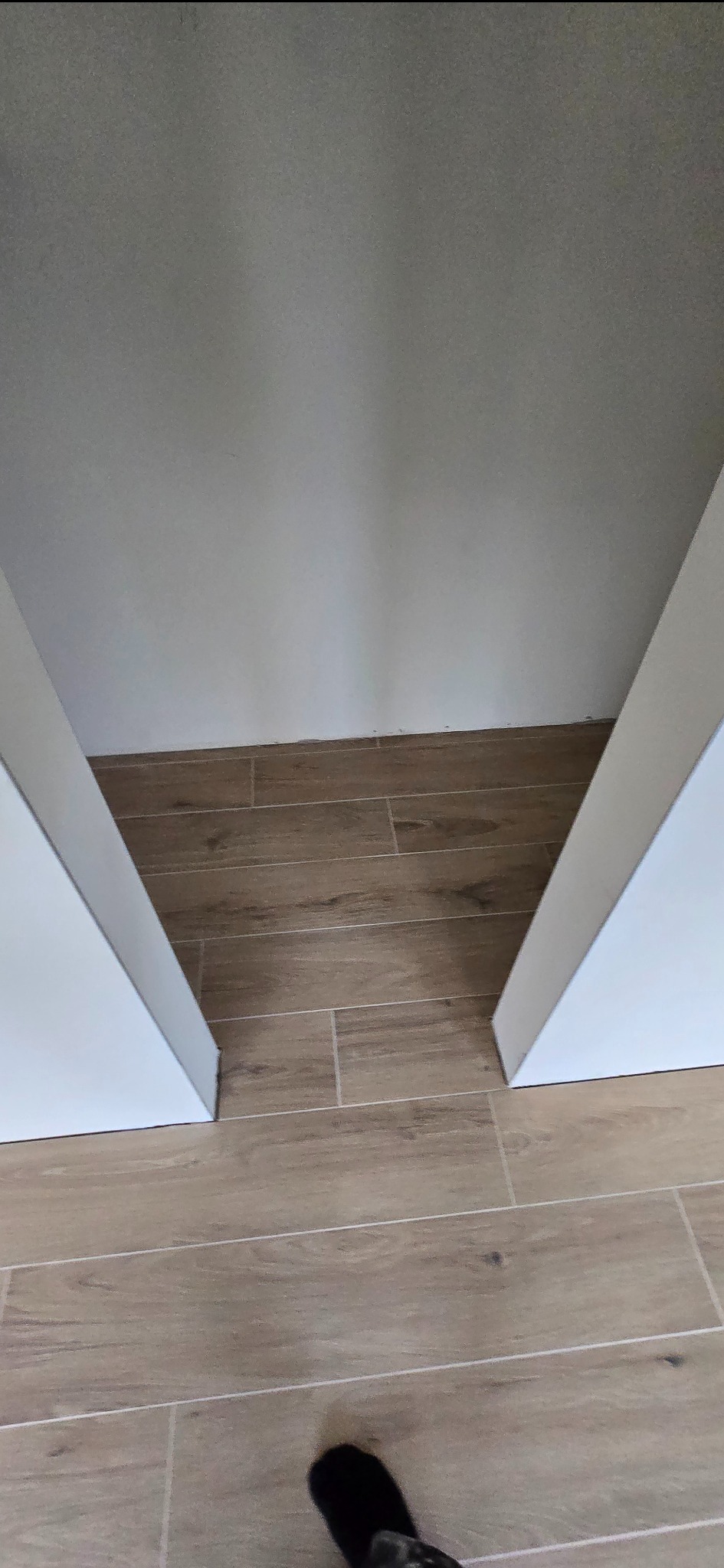 Ułożone płytki podłogowe imitujące drewno, widok z góry, fragment ściany i futryny drzwi. Widoczny cień osoby robiącej zdjęcie.