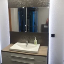 Nowoczesna łazienka z umywalką nablatową, szarą mozaiką nad umywalką i lustrem, oraz kabiną prysznicową widoczną w odbiciu lustra.