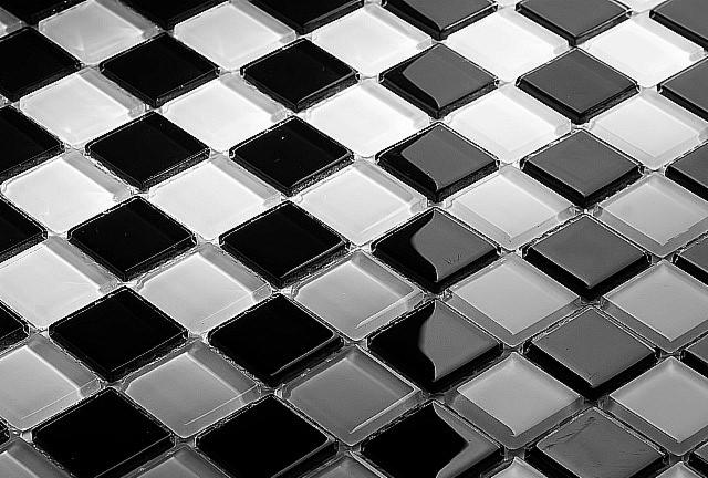 Czarno-biała mozaika z kwadratowych płytek szklanych, ułożonych w szachownicę, z widocznymi refleksami światła na powierzchni.
