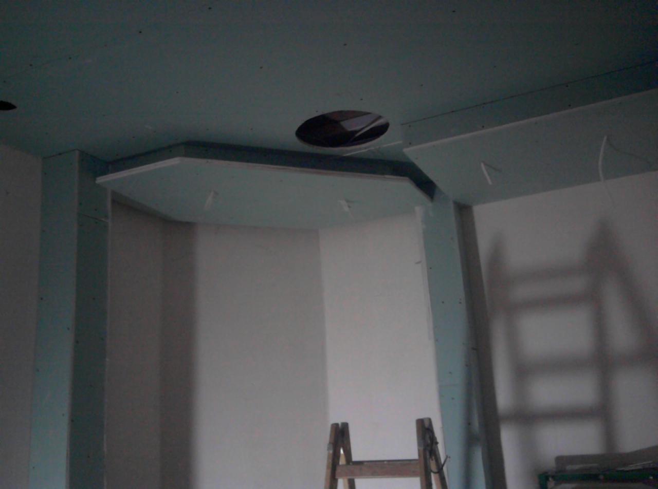Montaż podwieszanego sufitu z płyty gipsowo-kartonowej w narożnym pomieszczeniu, widoczne otwory na oświetlenie i elementy konstrukcyjne, drabina w tle.