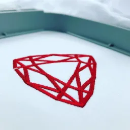 Czerwony geometryczny wzór diamentu wykonany ściegiem na białym materiale, umieszczony w ramce do haftowania.