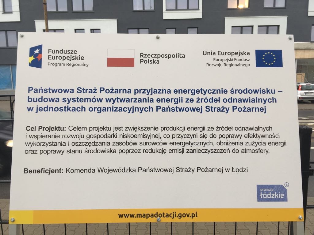 Tablica informacyjna o projekcie budowy systemów wytwarzania energii ze źródeł odnawialnych dla Państwowej Straży Pożarnej, z logo Funduszy Europejskich, Rzeczypospolitej Polskiej i Unii...