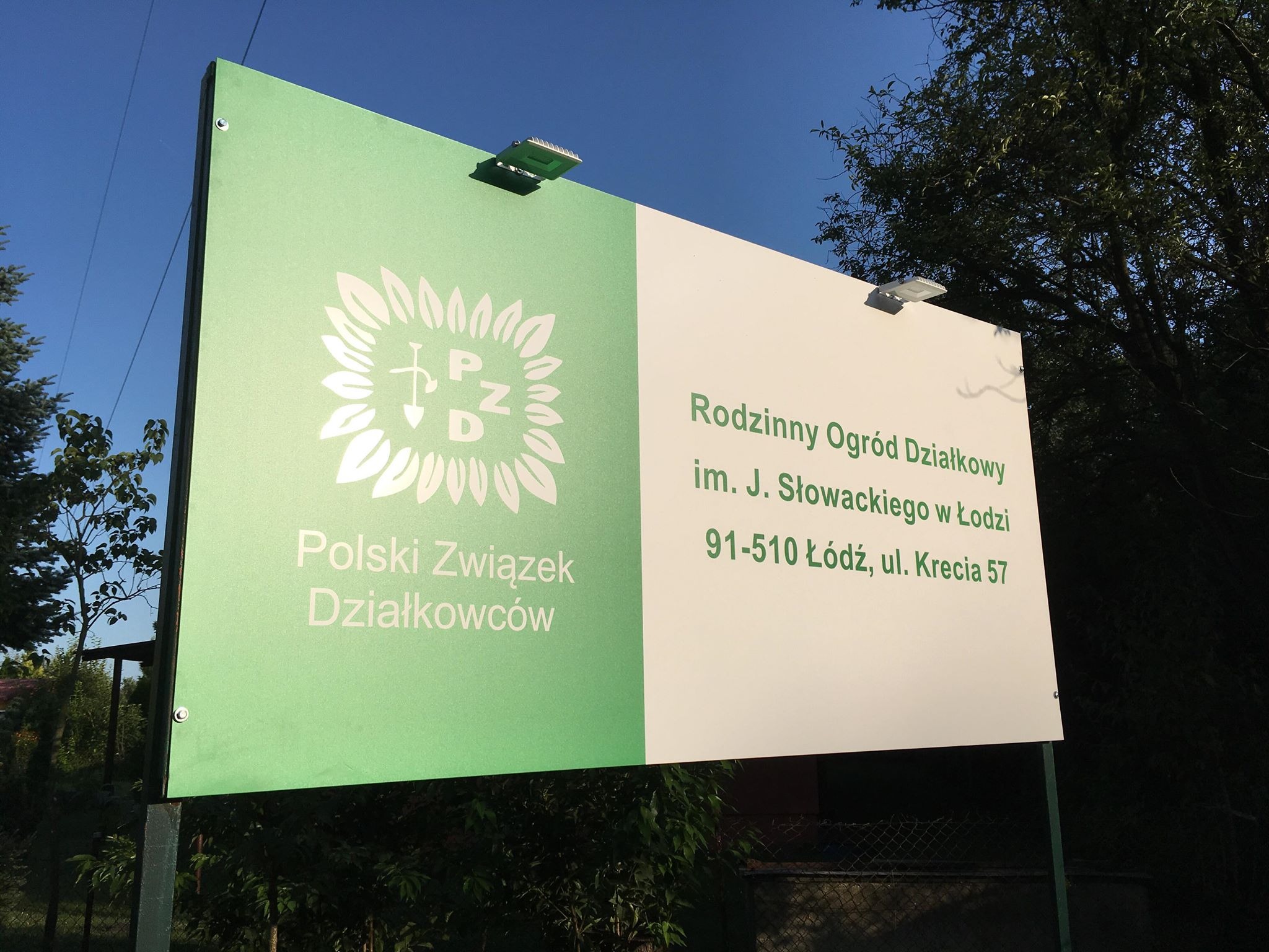 Zewnętrzny szyld informacyjny z logo i nazwą: Polski Związek Działkowców oraz Rodzinny Ogród Działkowy im. J. Słowackiego w Łodzi, umieszczony na zielono-białej tablicy z oświetleniem LED.