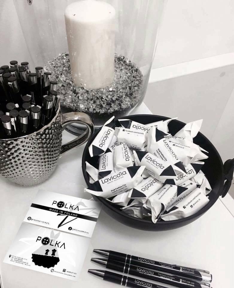 Aranżacja biurka z elementami identyfikacji wizualnej firm Polka i Lavicola: wizytówki, długopisy, cukierki reklamowe, świeca dekoracyjna i metalowy kubek na długopisy.