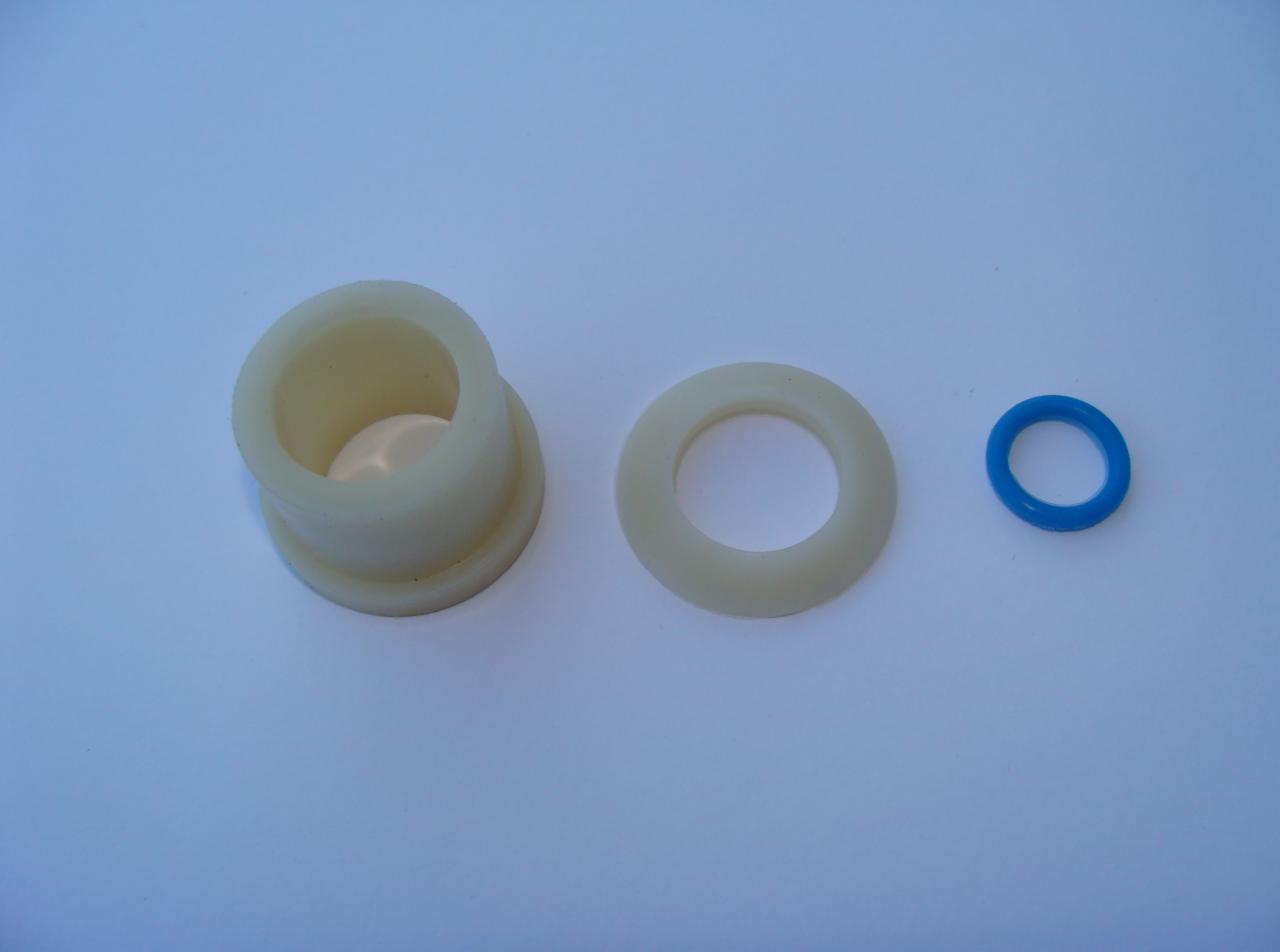 Trzy elementy hydrauliczne: tuleja z kołnierzem, uszczelka płaska i oring w kolorze niebieskim, ułożone na jasnoniebieskim tle.