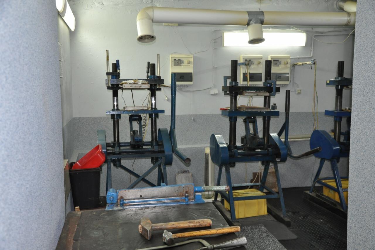 Warsztat z maszynami do obróbki materiałów, widoczne młotki, nożyce do blachy, wentylacja pod sufitem i skrzynki narzędziowe.