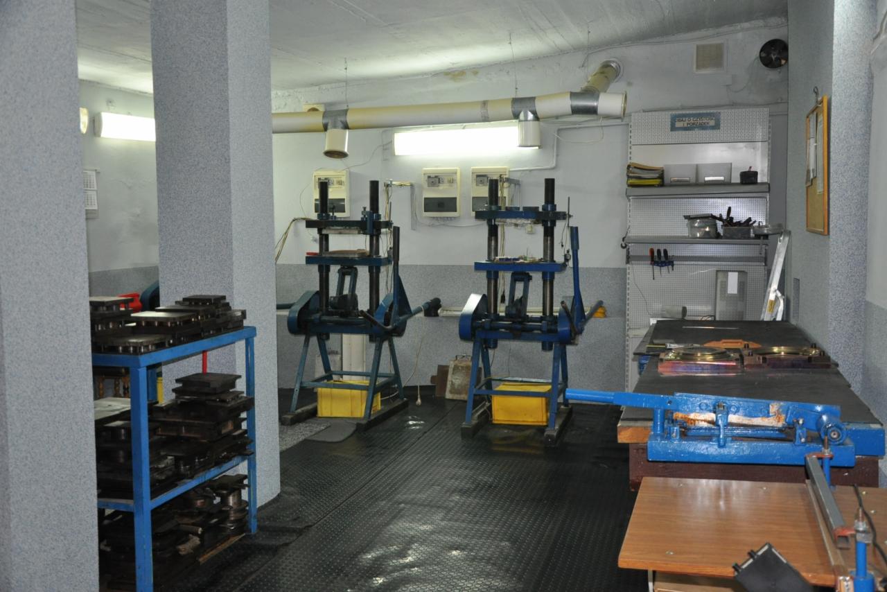 Warsztat z prasami hydraulicznymi, regałem z metalowymi płytami i stołem warsztatowym z narzędziami do obróbki metalu.