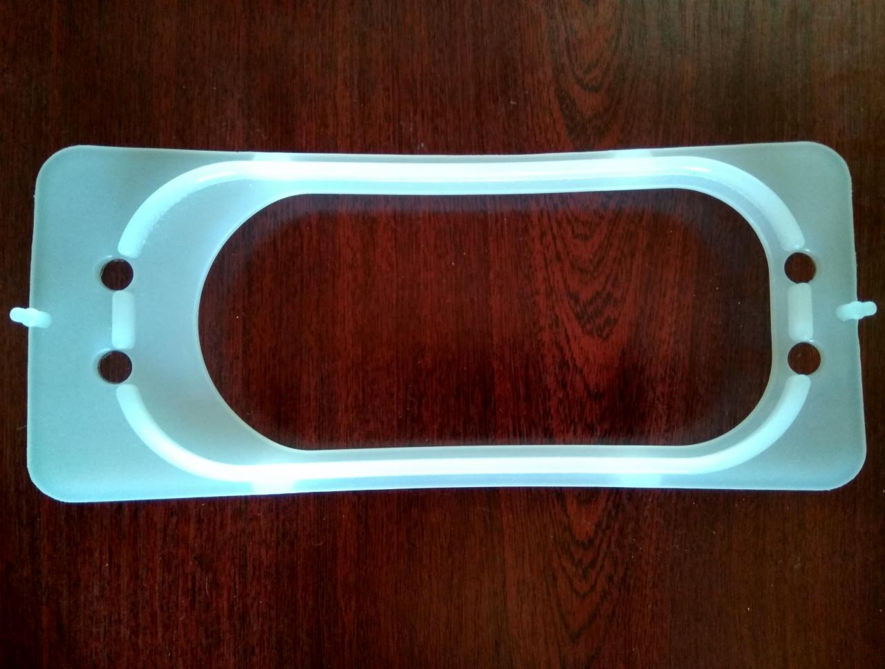 Uszczelka z tworzywa sztucznego z czterema otworami montażowymi na tle drewnianej powierzchni.