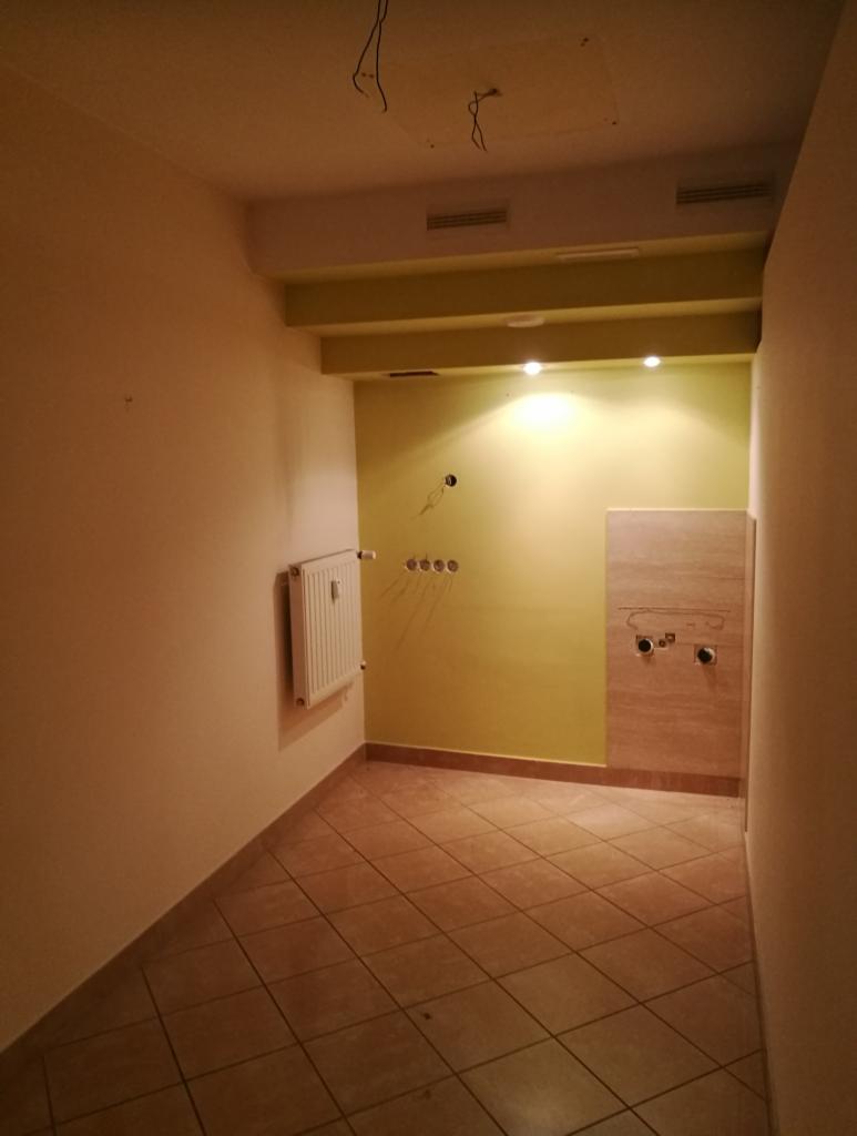 Wnętrze łazienki w trakcie remontu w Kaliszu, widoczne przygotowane instalacje wodno-kanalizacyjne, grzejnik i ułożone płytki podłogowe.
