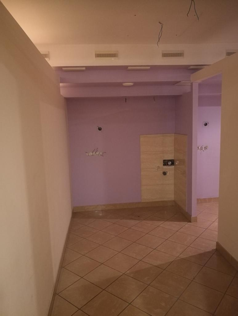 Wnętrze pomieszczenia w trakcie remontu, fioletowe ściany, brązowa podłoga z płytek, widoczne niedokończone instalacje elektryczne