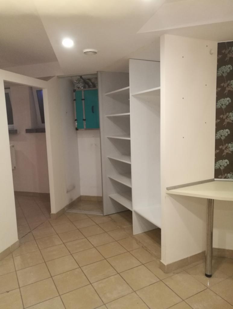 Wnętrze pokoju z nową, białą zabudową szafy z półkami, widoczny fragment biurka na metalowej nodze oraz instalacja wentylacyjna w tle.