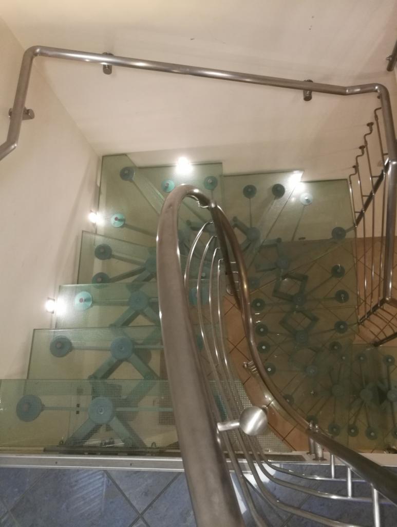 Szklane schody z metalowymi elementami konstrukcyjnymi widziane z góry, z widocznymi mocowaniami i poręczą ze stali nierdzewnej.