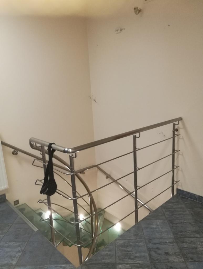 Szklane schody z metalową balustradą, na której wisi czarna saszetka, widok z góry.