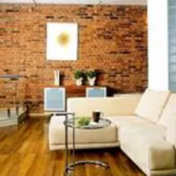 Salon po remoncie: ściana z cegły, jasna sofa, drewniana podłoga, stolik kawowy ze szklanym blatem, obraz na ścianie i rośliny doniczkowe.