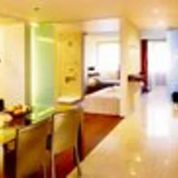 Jasne, nowocześnie urządzone wnętrze mieszkania z widokiem na salon i sypialnię. W części jadalnej stół z krzesłami, w tle drewniana podłoga i elementy dekoracyjne.