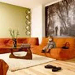 Jasne, przestronne wnętrze salonu po remoncie, z pomarańczową sofą modułową, drewnianym stolikiem kawowym na kremowym dywanie i dużym czarno-białym zdjęciem na ścianie. Dziecko siedzi na sofie.