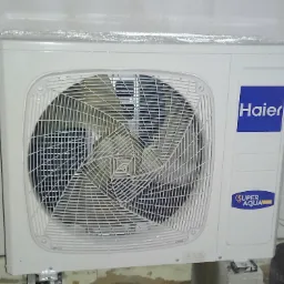 Zewnętrzna jednostka klimatyzacji Haier Super Aqua z folią ochronną na górze, zamontowana na betonowych wspornikach przy ścianie.