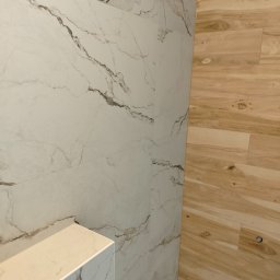 FRB Zbigniew Rzadzki - Ściana wyłożona płytkami imitującymi marmur z ciemnymi żyłami, sąsiadująca z panelami ściennymi imitującymi drewno. W dolnej części widoczne czerwone rury instalacji.