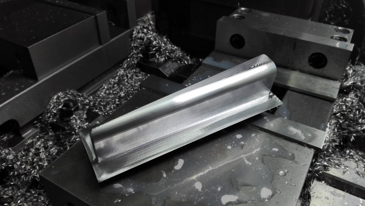 Obróbka metalu: Błyszczący, metalowy profil o przekroju kątownika, leżący na czarnej płycie roboczej, otoczony wiórami metalowymi. Widoczne ślady obróbki skrawaniem na powierzchni profilu.