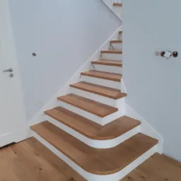 Nowoczesne schody drewniane z białymi podstopnicami w Wiśniowej, widoczne instalacje elektryczne na ścianie sugerują etap wykończeniowy.