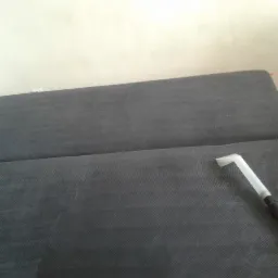 Dysza odkurzacza ekstrakcyjnego na szarej tapicerce sofy podczas czyszczenia, widoczne delikatne różnice w odcieniach materiału.