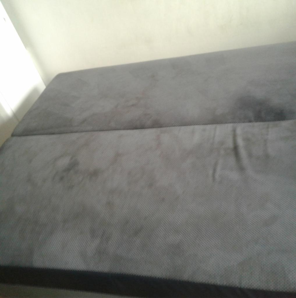 Szara, dwuczęściowa kanapa z widocznymi plamami na tapicerce, sfotografowana z góry w słabym oświetleniu.