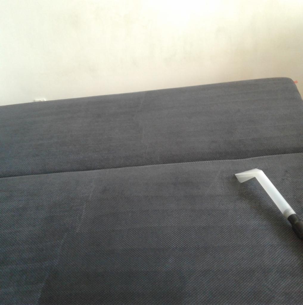 Dysza odkurzacza ekstrakcyjnego na szarej tapicerce sofy podczas czyszczenia, widoczne delikatne różnice w odcieniach materiału.
