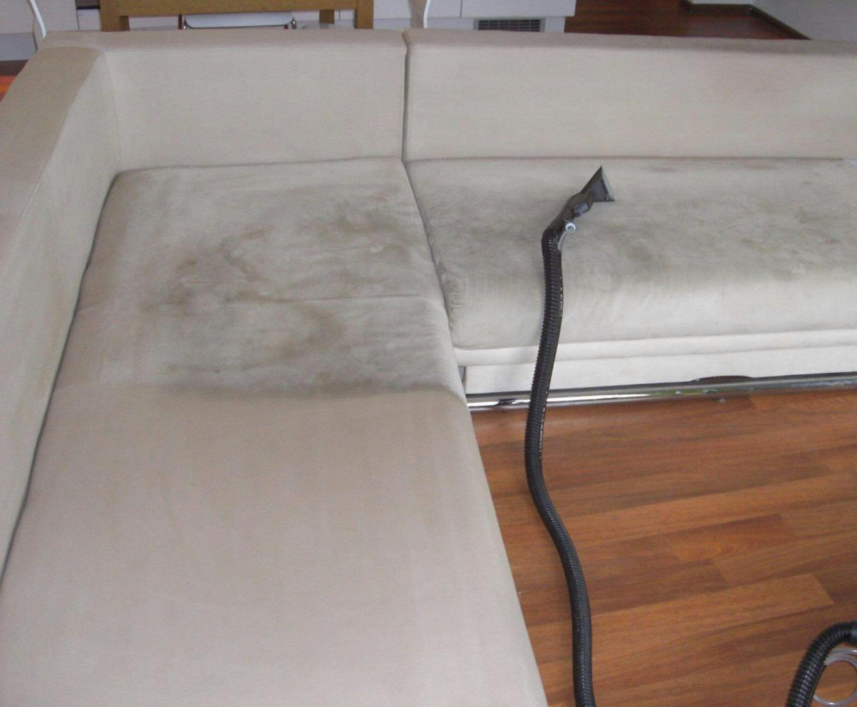 Fragment beżowej, narożnej kanapy z widocznymi plamami, częściowo wyczyszczonej za pomocą czarnego węża ssącego odkurzacza piorącego, ukazującego różnicę w wyglądzie przed i po czyszczeniu.