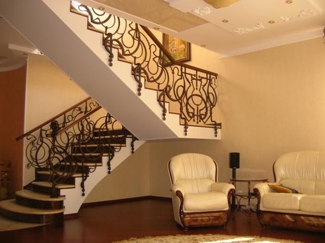 Eleganckie schody z kutą balustradą w jasnym wnętrzu, widoczne ozdobne elementy i drewniane poręcze.