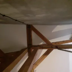 Kabel elektryczny przymocowany do sufitu klamrami, biegnący wzdłuż drewnianej konstrukcji stropu wewnątrz budynku.